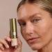 Model applying Mineral Powder Sunscreen SPF 30 by Sun Defense in Sheer, showcasing portable applicator and natural skin finish.