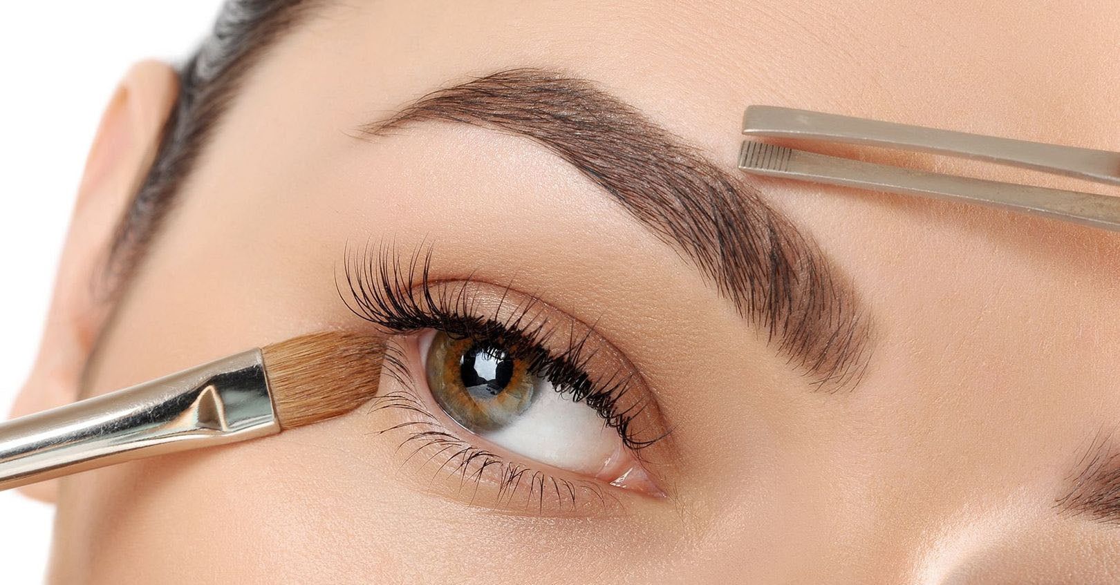 Close-up of eyebrow tinting with brush and tweezers